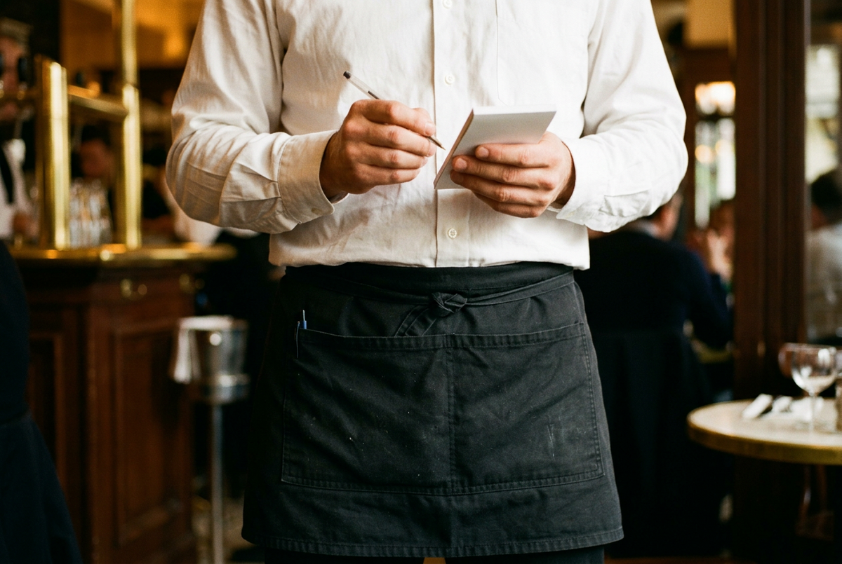 Serveur portant un tablier court noir à poches dans un restaurant